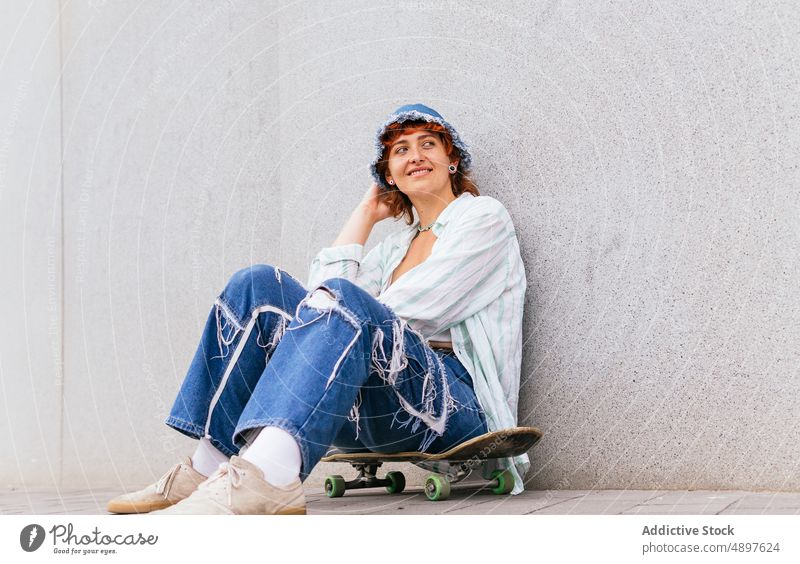 Frau sitzt Skateboard in der Nähe der Wand sitzen Skateboarderin Hobby sportlich Inhalt Glück Zeitvertreib Lächeln froh Freizeit Straße urban Aktivität genießen