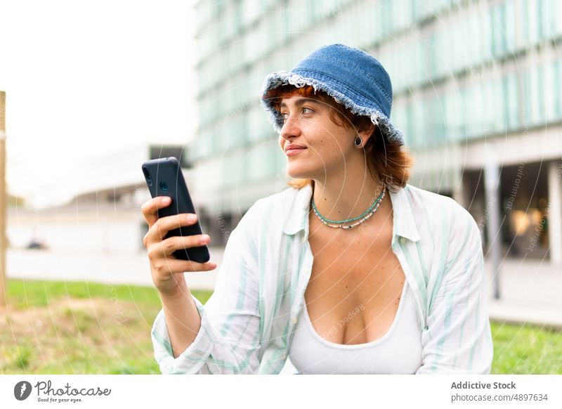 Lächelnde Frau, die auf einer Wiese auf ihrem Smartphone surft Browsen Rasen online Internet Straße Großstadt Talkrunde soziale Netzwerke Gebäude Surfen Gras