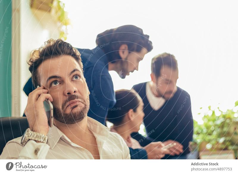 Genervter Mann, der in der Nähe von Kollegen mit seinem Smartphone spricht Arbeiter Telefonanruf Gespräch diskutieren Business verärgert unglücklich Büro