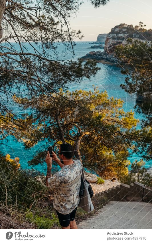Junger männlicher Tourist fotografiert das Meer auf einer Treppe in einer malerischen Bucht Mann fotografieren MEER Treppenhaus Reisender Smartphone Urlaub