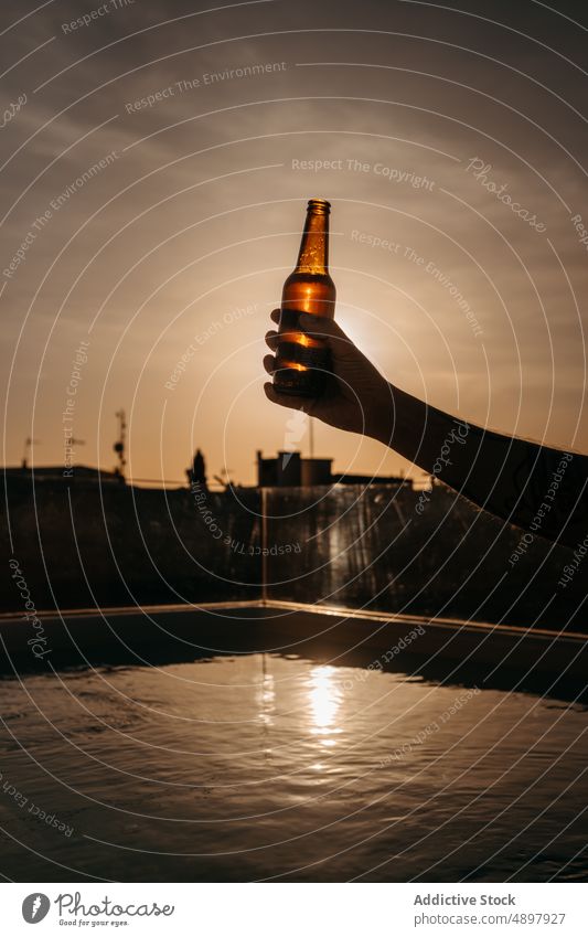 Silhouette eines anonymen Touristen, der eine Bierflasche im Pool hält Person Flasche Dachterrasse Sonnenuntergang trinken Kälte Feiertag Urlaub Alkohol zeigen