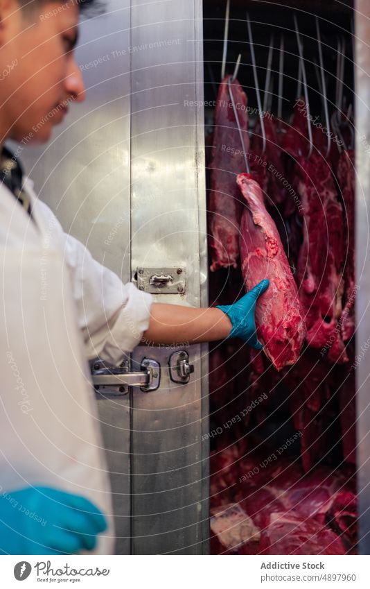 Männlicher Metzger prüft Fleisch im Kühlschrank Mann prüfen berühren Werkstatt bei der Arbeit frisch kalt männlich bewahren roh Haken professionell Industrie