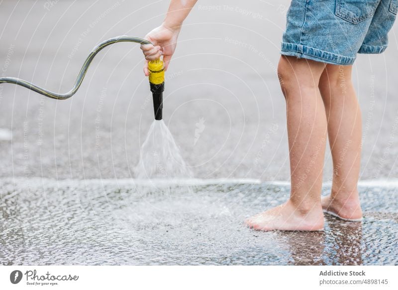 Junge wäscht Straße mit Schlauch Waschen Wasser Spray Bein Hand Beteiligung nass Bewegung kleiner Abschnitt Lifestyle Stehen außerhalb Selbstbedienung Aktivität