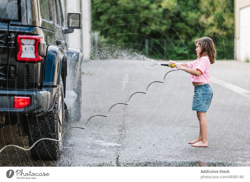 Nettes Mädchen mit Schlauch beim Waschen des Autos Spray Bewegung Sauberkeit Blick Wasser niedlich nass Pflege Lifestyle dreckig lässig wenig unschuldig