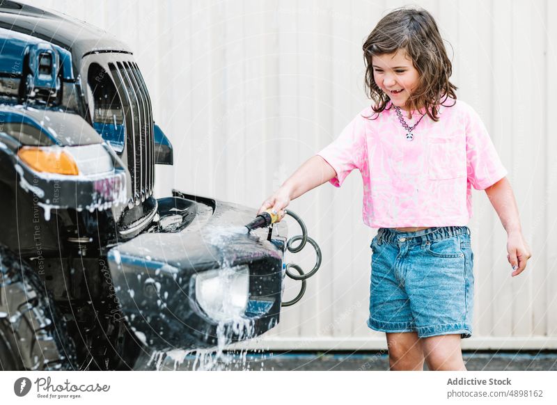 Mädchen in Casuals Waschen Auto mit Schlauch auf der Straße PKW Spray Glück Bewegung Sauberkeit Wasser niedlich nass Pflege Transport Lifestyle dreckig lässig