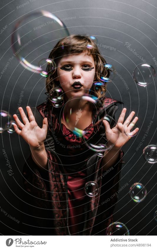Nettes kleines Mädchen im Gothic-Stil Outfit mit Seifenblasen im Studio Halloween Hexe feiern schmollende Lippen Kind Tracht Porträt gotisch Hexerei Karneval