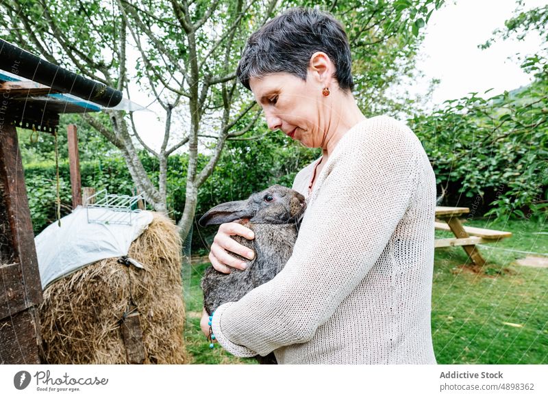 Glückliche Besitzerin hält niedlichen Hasen auf dem Lande Frau Kaninchen Landwirt Landschaft Garten Umarmen Hinterhof Tier heiter Lebensmitte Kurze Haare