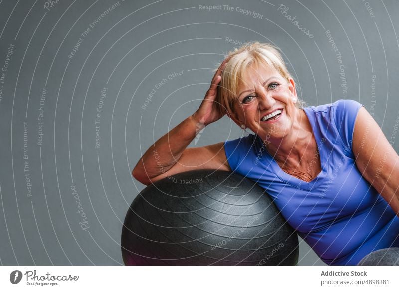 Lächelnde, fitte ältere Frau, die sich auf einen Fit-Ball stützt Passform-Ball Wegsehen Fitnessstudio sich[Akk] entspannen Lehnen Senior Pilates Übung Training