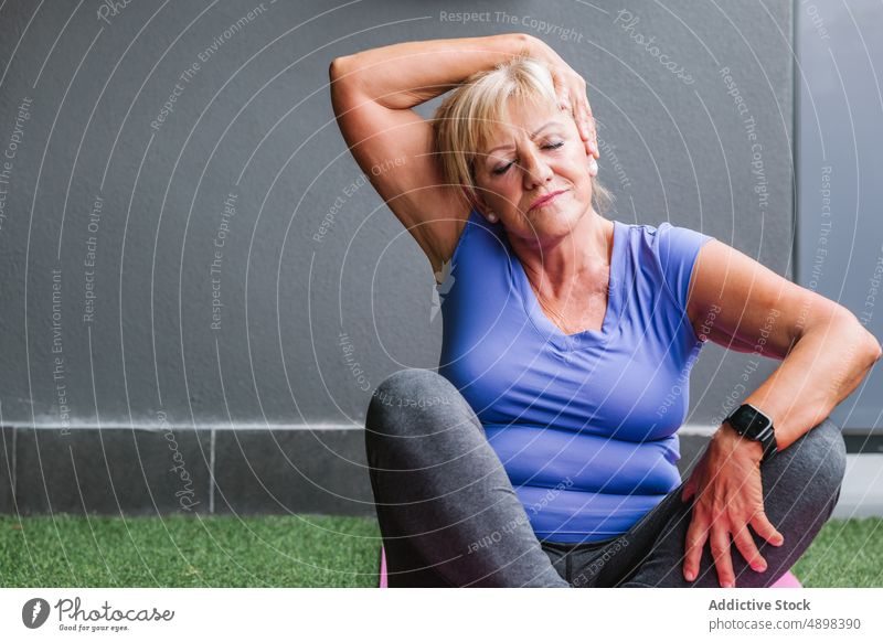 Fit Ältere Frau tun Hals Übung sitzen auf Yoga-Matte Senior strecken Unterlage Augen geschlossen passen Training Konzentration Sportbekleidung Gesundheit