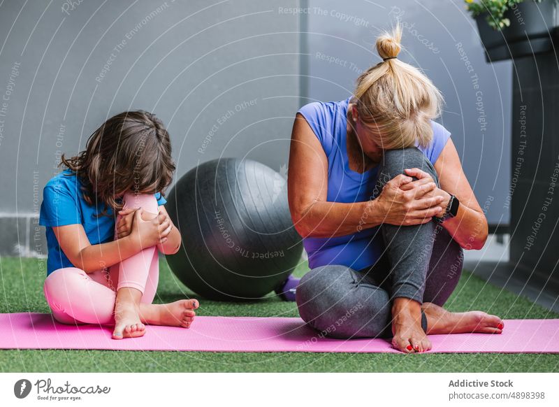 Ältere Frau und Mädchen üben Yoga auf einer Übungsmatte Training sich[Akk] entspannen Familie Bein Flexibilität umarmend Knie meditieren Lehre passen Gesundheit