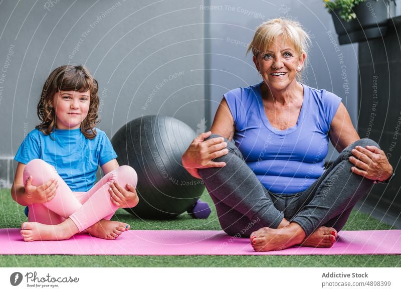 Lächelnde ältere Frau mit Mädchen, die Yoga auf der Matte macht Übung Training sich[Akk] entspannen Familie Flexibilität meditieren Lehre passen Gesundheit