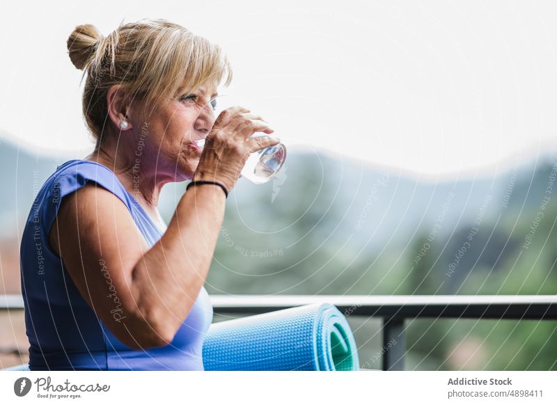 Fröhliche ältere Dame mit Yogamatte und Glas Wasser nach dem Training Senior Frau Beteiligung heiter Unterlage Lächeln Wegsehen trinken Erfrischung aktiv Körper