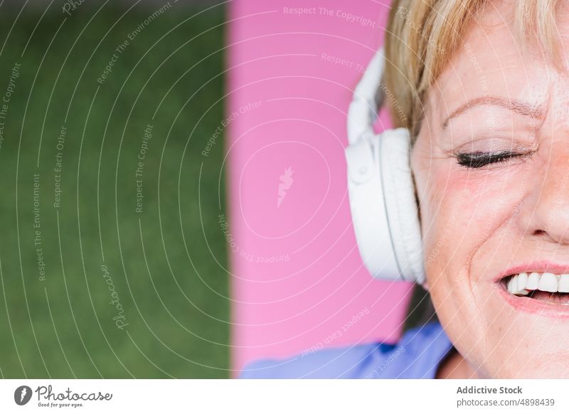 Ältere Frau hört Musik und meditiert auf einer Yogamatte Senior meditierend Augen geschlossen hören Lügen Unterlage Kopfhörer Lächeln Draufsicht Windstille