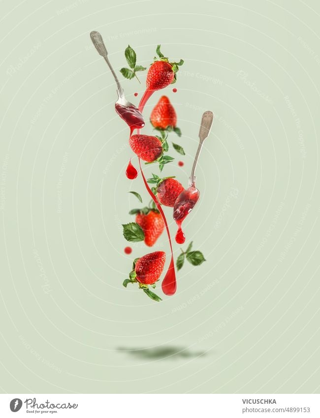 Fliegende Erdbeeren mit Marmeladenspritzern, Löffel mit tropfender Marmelade auf blassgrünem Hintergrund mit Schatten. fliegen erdbeeren platschen kreativ