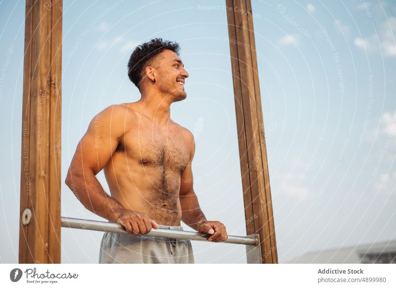 Sportler in der Nähe der Stange während eines Krafttrainings Mann calisthenics Lächeln Hand Pause hispanisch Reibung ruhen stehen sich[Akk] entspannen Training