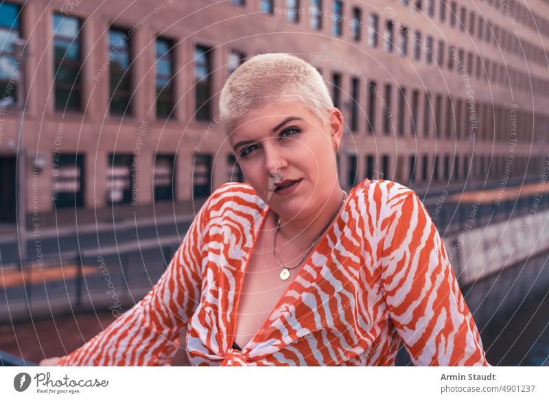 Macht und Schönheit: Porträt einer jungen Frau mit kurzen blonden Haaren auf einer Brücke in Berlin Atelier ernst selbstbewusst Behaarung stark Kraft kampfstark