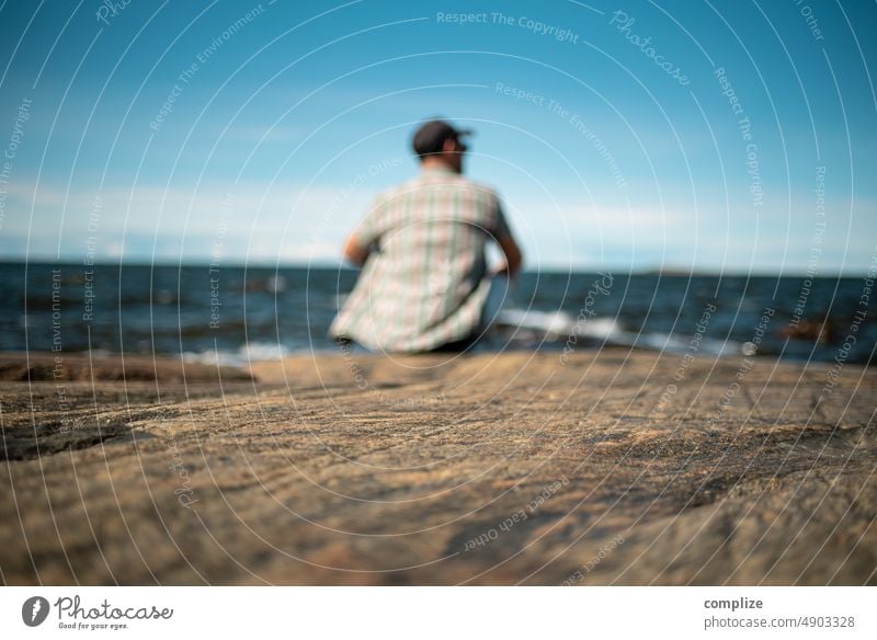 Mann sitzt auf einem Felsen am Meer bei Jakobstad/Pietarsaari entspannend relaxen Ruhe Sommer Urlaub schauen entspannt sitzen Stein Felsenküste Finnland