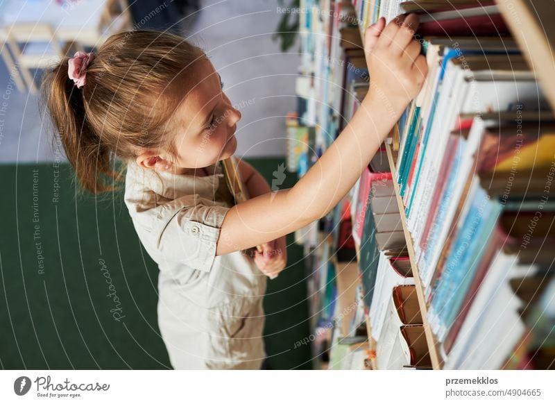 Schulmädchen schaut auf Bücherregal in Schulbibliothek. Kluges Mädchen wählt Literatur zum Lesen aus. Bücher in Regalen in einer Buchhandlung. Lernen aus Büchern. Zurück zur Schule. Schulbildung