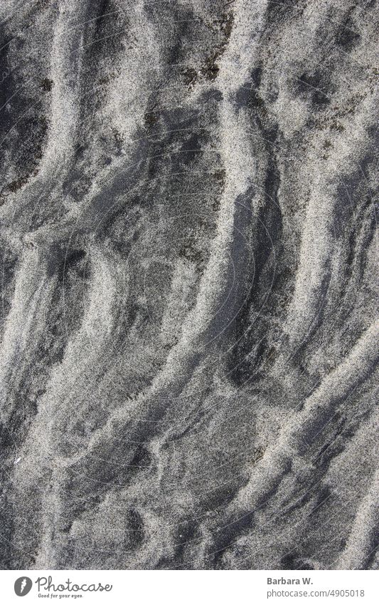 Ein Muster, das durch Wellen auf dem Sand eines Strandes entsteht. Hintergrund Nahaufnahme außerhalb natürliches Licht Sandstrandmuster Textur des Sandes grau