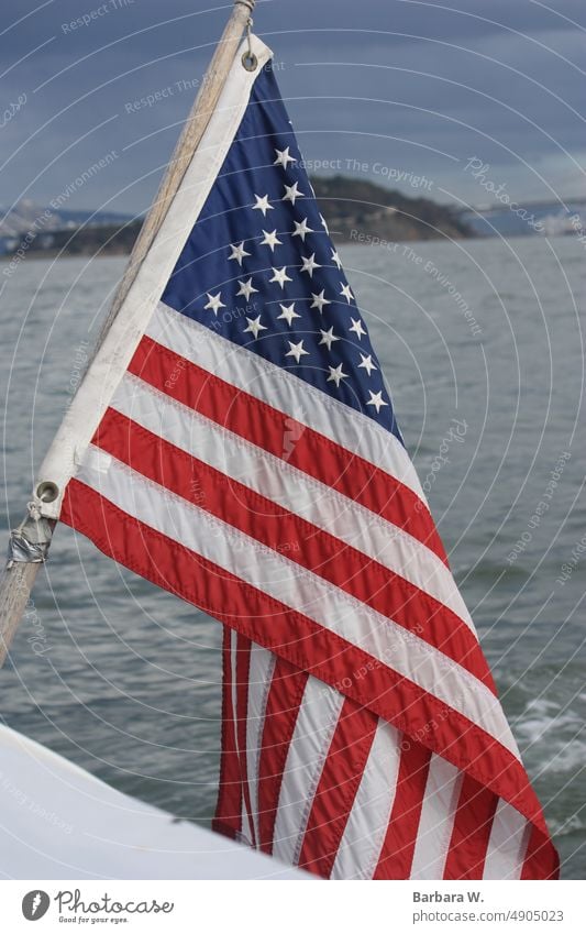 Vom Rand eines Bootes aus sieht man die amerikanische Flagge mit dem Gefängnis von Alcatraz und der Bucht von San Francisco im Hintergrund. Stars and Stripes