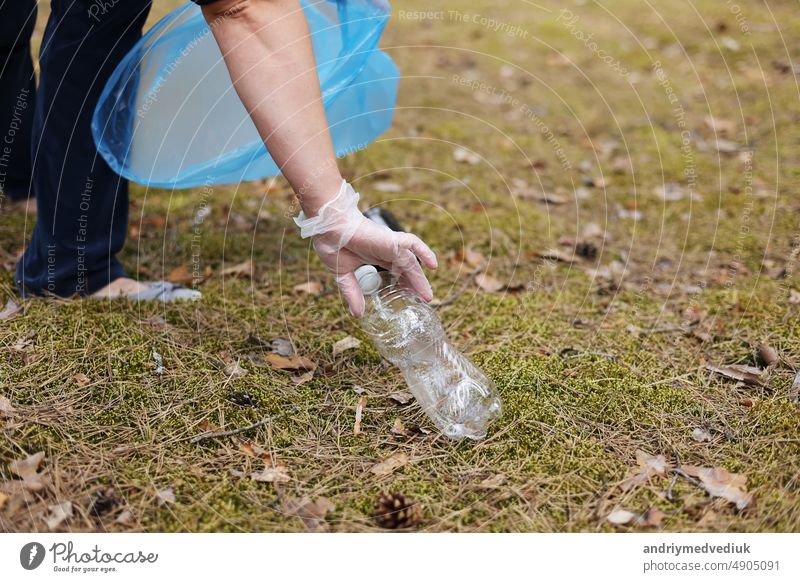 Eine Frau mit Handschuhen sammelt gebrauchte Plastikflaschen ein und steckt sie in einen blauen Müllsack. Ein Freiwilliger säubert den Park an einem sonnigen, hellen Tag. Aufräumen, Verschmutzung, Ökologie und Plastikkonzept