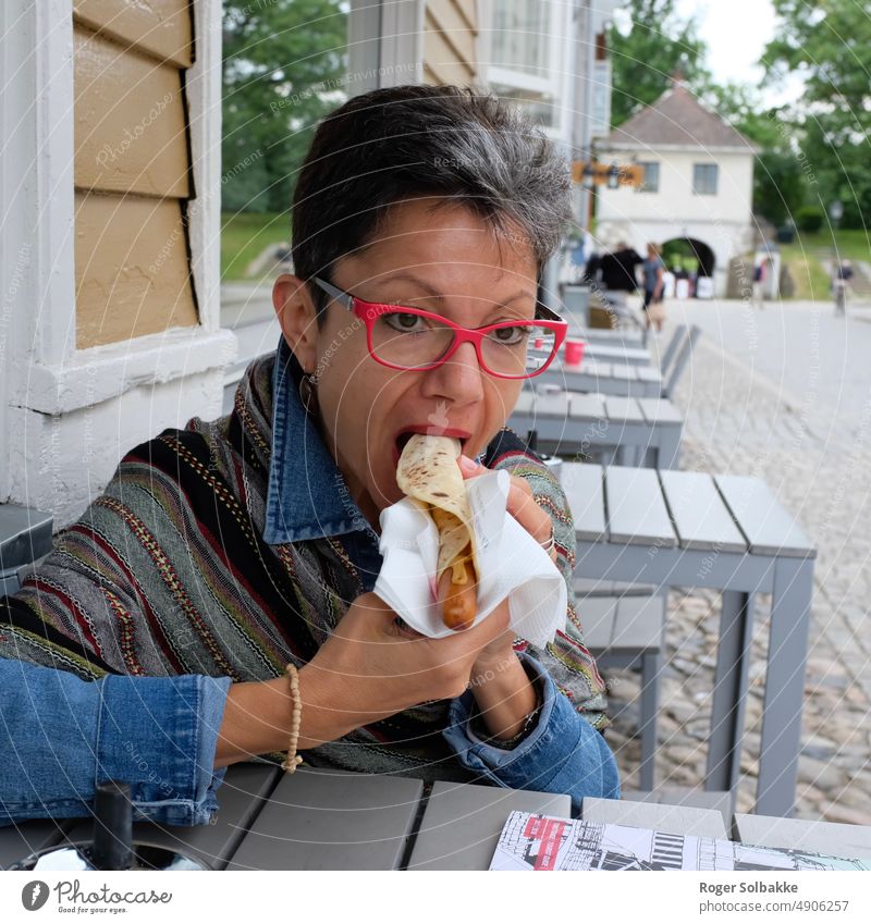 Frau isst Wurst in einer Tortilla, in einem Restaurant im Freien Farbe Wurstbrot Wurstwaren Tabelle Straße Außenrestaurant Essen Dame Rote Brille Schwarzes Haar