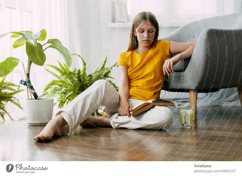 Eine junge Studentin sitzt auf dem Boden und liest ein Buch. Sie genießt die Lektüre an einem Wochenende oder bereitet sich auf den Unterricht in der Schule oder an der Universität vor. Zurück zur Schule, Vorbereitung auf den Unterricht, Freizeit