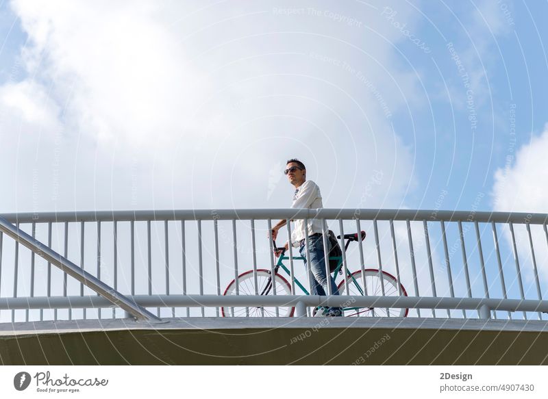 junger Hipster, der mit einem Fahrrad mit festem Gang auf einer Stadtbrücke fährt Sonnenbrille Stehen Himmel Mann Brücke Person im Freien Großstadt reisen