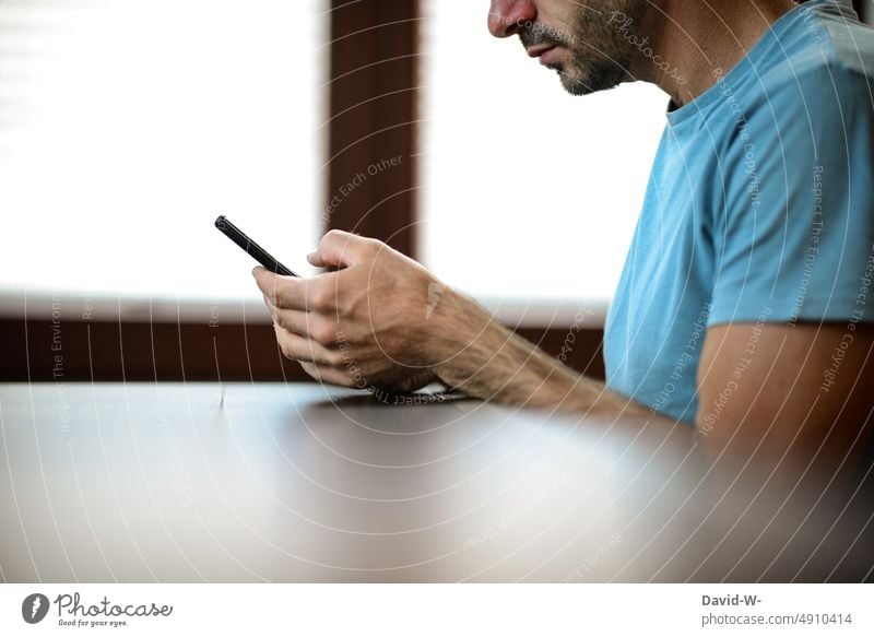 Mann sitzt am Tisch und schaut auf sein Handy benutzen tippen Finger anonym Smartphone Technik & Technologie Mobile Hände Abhängigkeit sucht