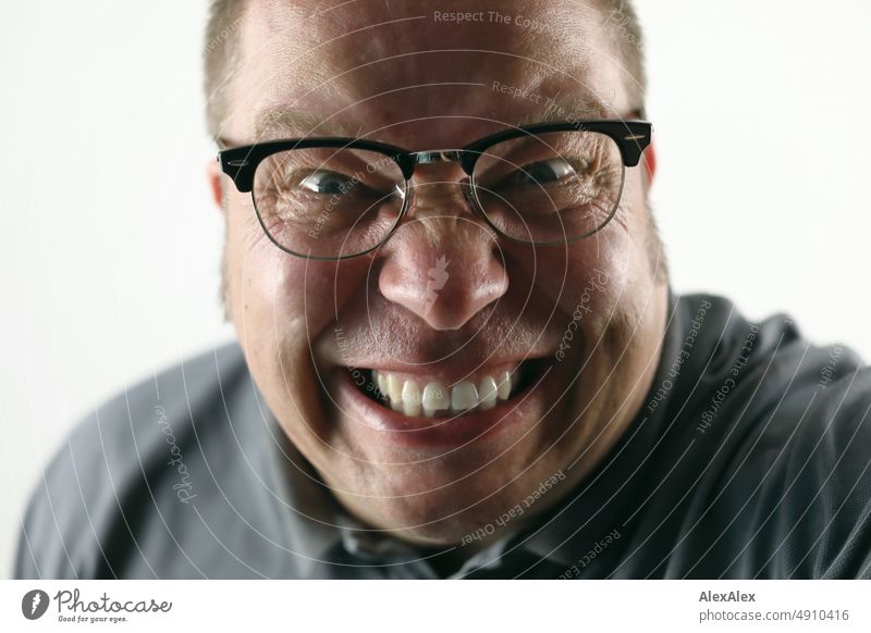 Sehr nahes Portrait eines Mannes, der wie wahnsinnig in die Kamera grinst und schaut - und eine schwarz umrandete Vintage- Brille trägt wild Spaß Freude
