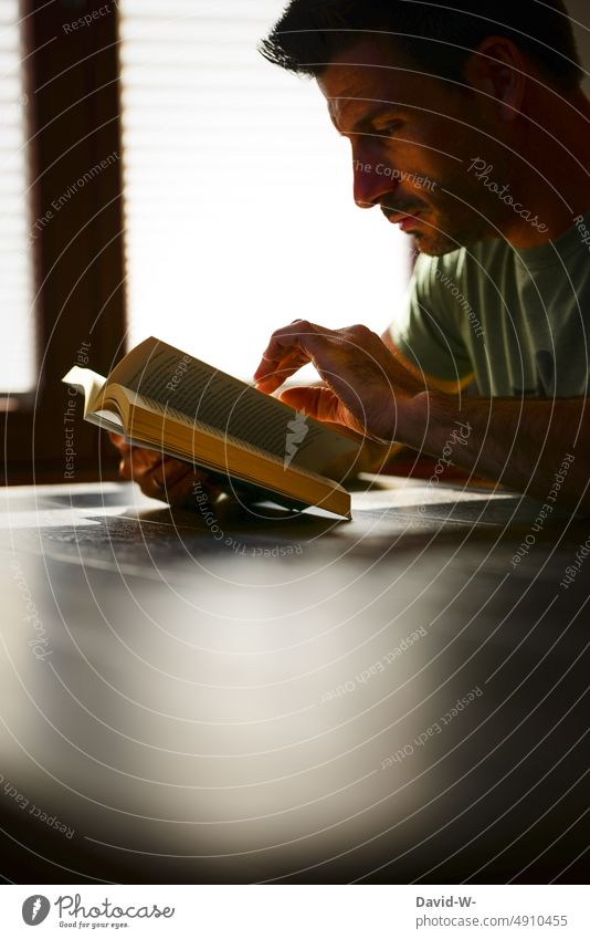 lesen - Mann mit Buch in der Hand Gesicht vertieft lernen Roman Bildung Literatur Wissen konzentriert Tisch Sonnenlicht Schatten Licht Schule