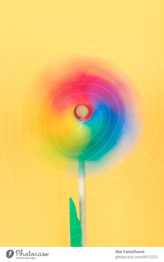 Bewegtes farbiges Windrad auf gelbem Hintergrund. Vertikales Foto. Thematisch lgtbq. Farbe Kunststoff Sommer Spielzeug Windmühle Spaß Rad blau rot Glück