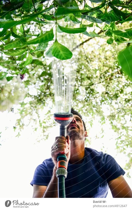 Mann wässert Blumen im Garten wässern Wasserschlauch Sommer trockenperiode wasserverbrauch Gartenarbeit Pflanzen gießen Gärtner