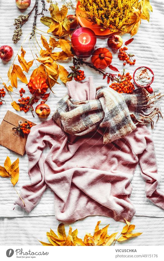 Herbst Lebensstil mit gestrickten Pullover, orange Blätter, Kerzen, Kürbisse und heiße Schokolade auf weißem Stoff Hintergrund. Gemütliche saisonale Mode Konzept mit Pullovern und Dekoration