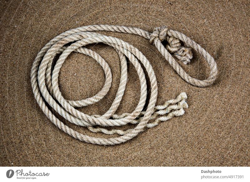 Altes Seil an einem sandigen Küstenstrand alt Rolle altes Seil gerolltes Seil weiß grau Sand braun Knäuel Schlinge Öhr Stränge Strand Küstenstreifen Seeküste