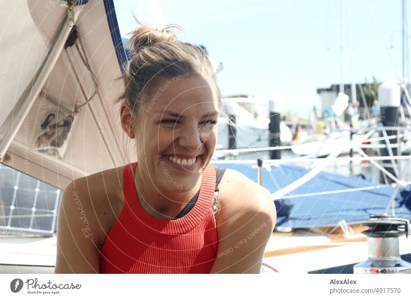 Junge, schöne Frau sitzt auf einem Segelboot und lächelt Lifestyle Gegenlicht gesund sportlich schlank ästhetisch jugendlich anmutig selbstbewußt authentisch