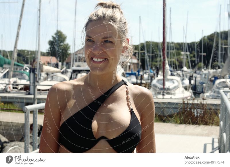 Junge, schöne Frau in schwarzem Bikini am Pier eines Segelboothafens an der Ostsee Lifestyle Gegenlicht gesund sportlich schlank ästhetisch jugendlich anmutig
