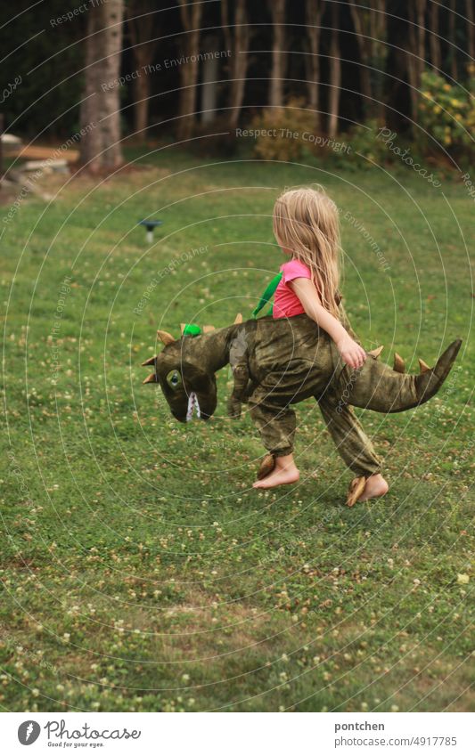 Ein als Dinosaurier verkleidetes kleines Kind läuft durch einen Garten. Spielen dinosaurier verkleidung kostüm garten laufen spielen fasching karneval Kindheit