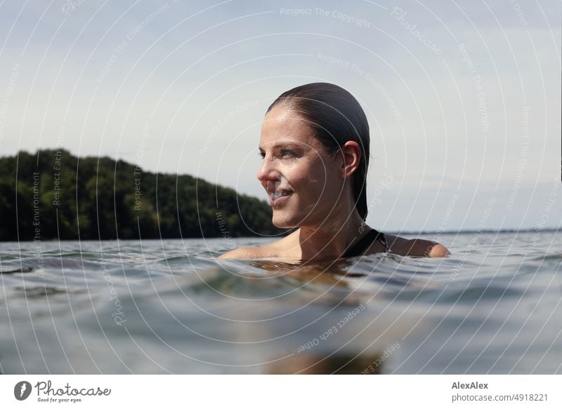 Junge, schöne Frau im flachen Wasser in der Ostsee schaut zur Seite und lächelt Lifestyle Gegenlicht gesund sportlich schlank ästhetisch jugendlich anmutig