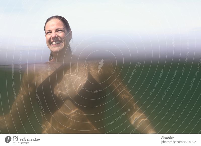 Junge, schöne Frau im flachen Wasser in der Ostsee schaut zur Seite und lächelt - Sichtbarkeit Teil- Unterwasserbild Lifestyle Gegenlicht gesund sportlich