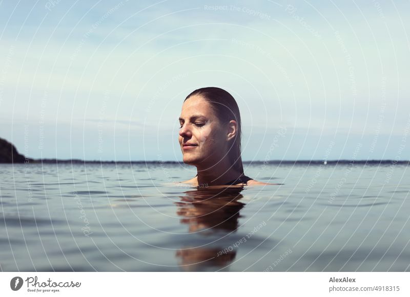 Junge, schöne Frau im flachen Wasser in der Ostsee lächelt zufrieden mit geschlossenen Augen Lifestyle Gegenlicht gesund sportlich schlank ästhetisch jugendlich