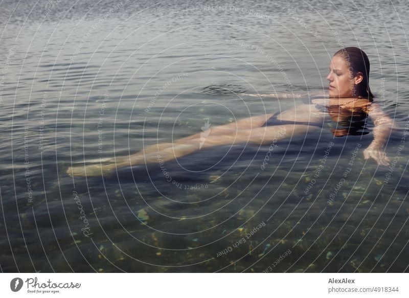 Junge, schöne Frau liegt im flachen Wasser der Ostsee und schwimmt auf der ruhigen See Lifestyle Gegenlicht gesund sportlich schlank ästhetisch jugendlich