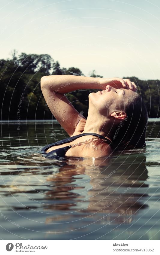Junge, schöne Frau im flachen Wasser in der Ostsee lächelt und streicht sich durch die nassen Haare Lifestyle Gegenlicht gesund sportlich schlank ästhetisch