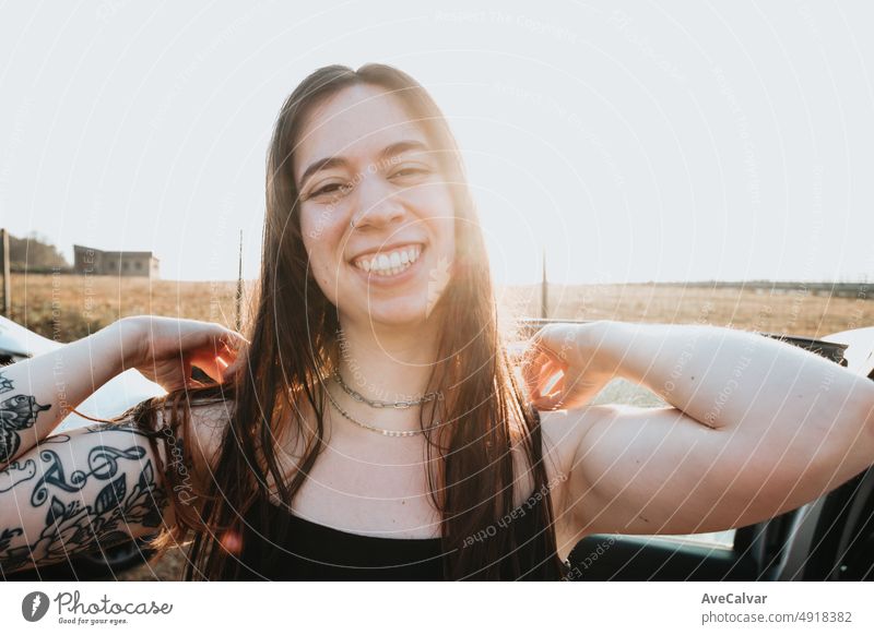 Porträt eines super glücklich lächelnde junge Frau mit Tattoos berühren sein Haar während eines Sonnenuntergangs. Sorglos Urlaub freie Zeit Konzept. Freiheit und Freiheit Konzept. Gen Z im Freien Spaß. Neues Leben neue Tage.