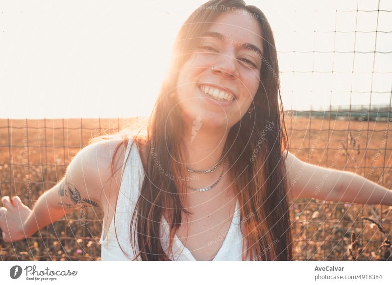 Super glückliche und positiv lächelnde junge Frau mit Tattoos, die sich an einem Zaun ausruht, während sie die Augen schließt und sich entspannt. Sorglos Urlaub freie Zeit Konzept. Freiheit und Freiheit Konzept. Gen Z im Freien Spaß.