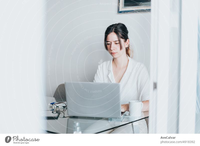 Kreative junge Frau, die in ihrem Studio aus der Ferne am Laptop arbeitet und dabei konzentriert aussieht. Sie tippt und sucht auf dem Laptop im Internet. Auf der Suche nach einem neuen Job freiberuflich. Home-Office-Konzept.