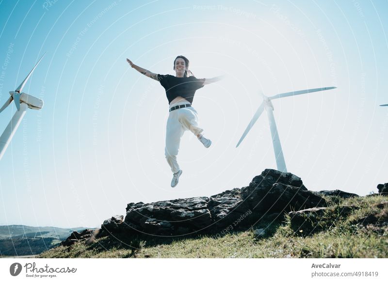 Junge Frau springt in die Freiheit, umgeben von elektrisch betriebenen Windrädern. Neue Energiequellen Konzept. Junge bewusste Menschen, recyceln, wiederverwenden, retten den Planeten Konzept. Nachhaltige Welt