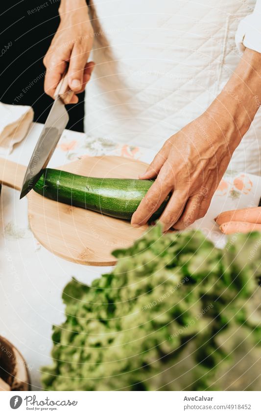Alte Frau schneidet frische Zucchini in der Küche, Nahaufnahme, Vorbereitung frischer gesunder Lebensmittel mit Gemüse. Rustikale Küche Kochen von Chefkoch gemacht. Vorbereiten von Zutaten für eine Bio-Mahlzeit. Diät und die Pflege von Lebensmitteln.