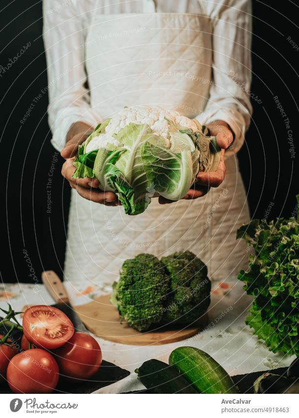 Close up Bild einer alten Frau Kochen Koch packt Blumenkohl und zeigt in die Kamera, bevor sie in einem gesunden food.Rustic Küche Kochen von Koch gemacht. Die Vorbereitung Zutat für eine Bio-Mahlzeit.