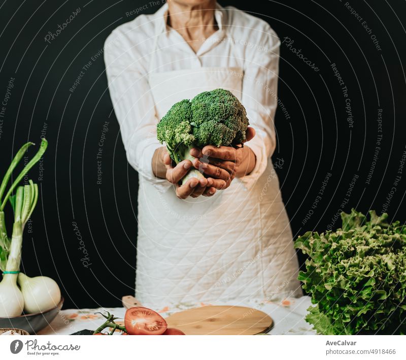 Close up Bild einer alten Frau Kochen Koch packt Brokkoli und zeigt in die Kamera, bevor sie in einem gesunden food.Rustic Küche Kochen von Koch gemacht. Die Vorbereitung Zutat für eine Bio-Mahlzeit.